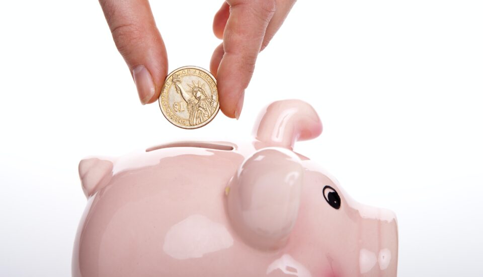 A hand putting a coin into a pink piggy bank.