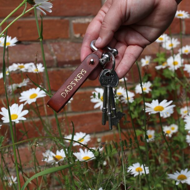 A person holding a key chain in front of daisies.