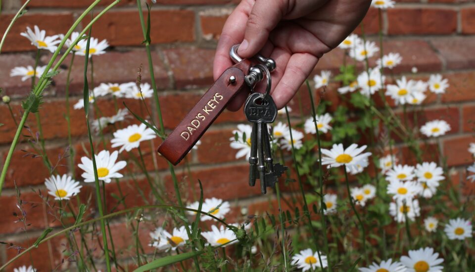A person holding a key chain in front of daisies.